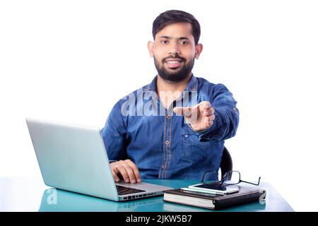 Geschäftsmann zeigt imaginäres Produkt auf der Hand und lächelt vor dem Laptop Stockfoto