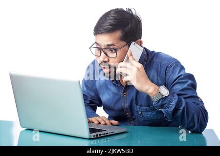Überraschender Mann, der auf dem Mobiltelefon sprach und den Computerbildschirm im isolierten Hintergrund ansah Stockfoto