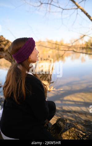 Ein Porträt einer Frau mit natürlichem blondem Haar, die an einem Frühlingstag mit einem violetten Haarreif in die Ferne auf einen Fluss blickt Stockfoto