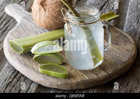 Ein Glas Kokoswasser mit Aloe Vera Stücken, auf einem rustikalen Holzbrett. Stockfoto