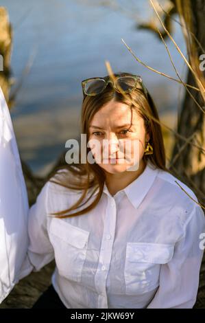 Eine selbstbewusste Frau im Freien vor einem Fluss sitzt auf einem Ast Stockfoto