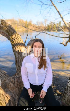 Eine selbstbewusste Frau im Freien vor einem Fluss sitzt auf einem Ast Stockfoto