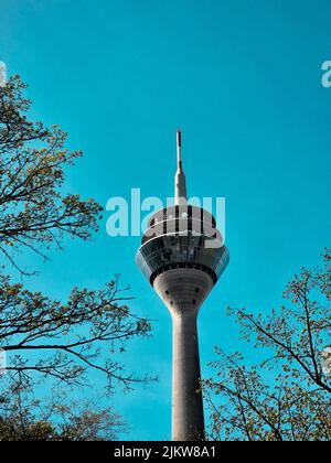 Eine vertikale Aufnahme des Rheinturms an einem blauen Himmelstag mit Bäumen in der Umgebung Stockfoto