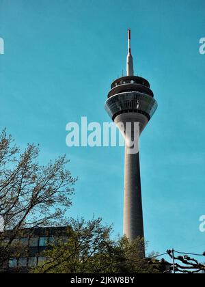 Eine vertikale Aufnahme des Rheinturms an einem blauen Himmelstag mit Bäumen in der Umgebung Stockfoto