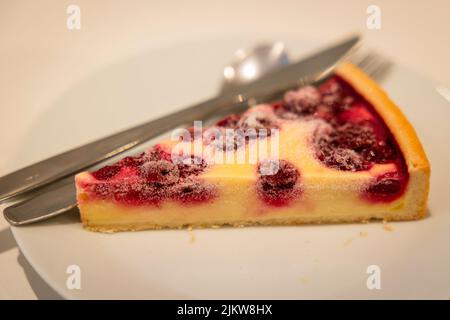 Ein leckerer Kuchen, der mit Himbeeren gebacken und auf einem weißen Teller auf einem verschwommenen Hintergrund serviert wird Stockfoto