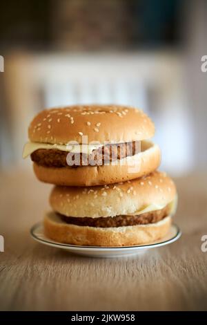 Eine vertikale Aufnahme von zwei Burgern übereinander auf einem Holztisch Stockfoto