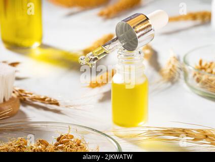 Eine konzeptionelle Zusammensetzung von ätherischem Weizenöl, einer Badebürste und Weizenkeimen auf einem Marmortisch. Eine Flasche Körperöl mit einem Tropfer. Weizenserumöl Stockfoto