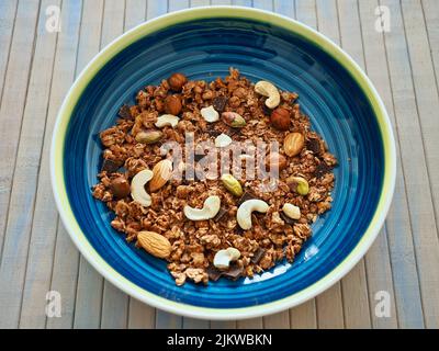 Müsli mit Nüssen in einer bunten Schüssel auf einem abgewaschenen Holztisch Stockfoto