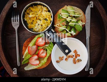 Blick von oben auf Rühreier in einer Pfanne, Erdbeeren und Salat auf einem Toast und Avocado auf einem Toast Stockfoto