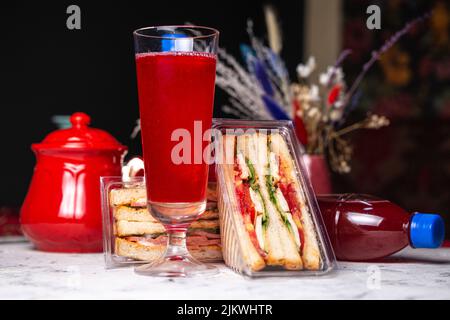 Sandwich mit Füllung in einer Plastikverpackung und einem Getränk auf dem Tisch. Stockfoto