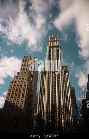 Ein vertikaler niedriger Winkel der Woolworth-Gebäude in New York in der Sonne unter einem bewölkten Himmel Stockfoto