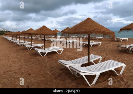 Eine Reihe von Strandliegen an einem leeren Strandresort in Südeuropa an einem bewölkten Tag ohne Touristen. Stockfoto