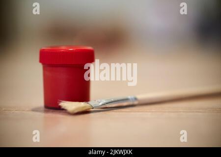 Eine Nahaufnahme eines roten Farbbehälters und eines Pinsels auf einem Holztisch Stockfoto