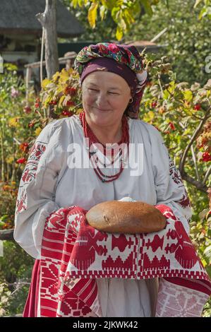 Die nicht identifizierte alte Frau in ukrainischer Nationaltracht überreicht bewunderten Gästen Brot in Salz traditionelle slawische Begrüßung in Kiew, Ukrai Stockfoto