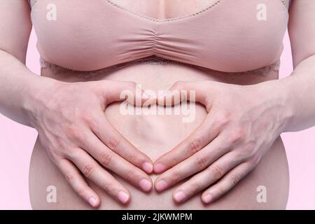 Eine Frau in ihrer späten Schwangerschaft, die ein Herz mit Händen auf ihrem Bauch zeigt Stockfoto