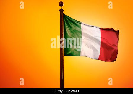 Die Nationalflagge Italiens auf einem Fahnenmast isoliert auf einem orangen Hintergrund Stockfoto