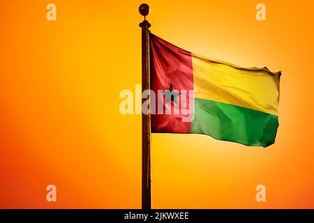 Die Nationalflagge von Guinea-Bissau auf einem Fahnenmast isoliert auf einem orangen Hintergrund Stockfoto