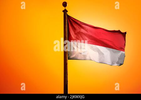 Die Nationalflagge Indonesiens auf einem Fahnenmast, isoliert auf einem orangefarbenen Hintergrund Stockfoto