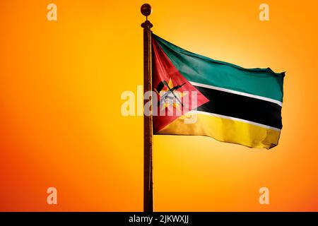 Die Nationalflagge von Mosambik auf einem Fahnenmast isoliert auf einem orangen Hintergrund Stockfoto