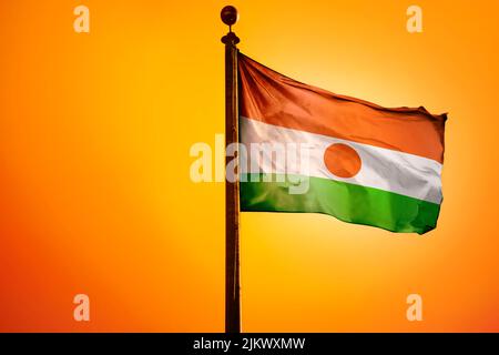 Die Nationalflagge Nigers auf einem Fahnenmast, isoliert auf einem orangen Hintergrund Stockfoto