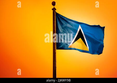 Die Nationalflagge der Heiligen Lucia auf einem Fahnenmast isoliert auf einem orangen Hintergrund Stockfoto