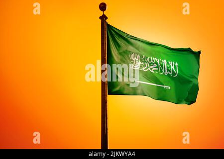 Die Nationalflagge Saudi-Arabiens auf einem Fahnenmast, isoliert auf einem orangefarbenen Hintergrund Stockfoto