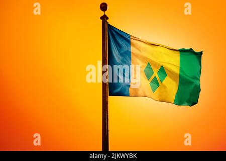 Die Nationalflagge von St. Vincent und den Grenadinen auf einem Fahnenmast isoliert auf einem orangen Hintergrund Stockfoto