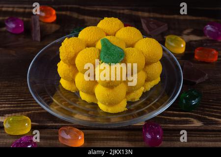 Appetitliche, attraktive gelbe Mango-Mousse-Torte auf dunklem Holztisch mit verstreuten Süßigkeiten und Pralinen, selektiver Fokus. Stockfoto