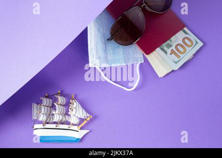 Spielzeug Schiff Sonnenbrille und Reisepass mit Dollar auf lila Hintergrund mit Kopieplatz. UrlaubsGrußkarte mit Schiff. Reisekonzept. Minimalismus trave Stockfoto