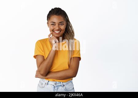 Schöne afroamerikanische Mädchen, Teenager lächelnd und Blick neben Logo, trägt gelbe T-Shirt, weißen Hintergrund Stockfoto