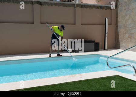 Betreiber Reinigung eines Schwimmbades mit einer Schmetterlingsfalle, mit Kunstrasen und einer Dusche im Hintergrund. Stockfoto