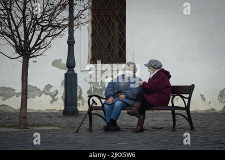 Óbuda, Ungarn - Mär 21 2021: Zwei alte Damen sitzen auf einer Bank und plaudern während der Covid-Zeit, maskiert Stockfoto