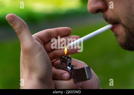 Junger bärtiger Mann zündete eine Zigarette mit einem Metallfeuerzeug aus der Nähe an Stockfoto