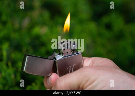 Budapest, Ungarn - 04 2022. Mai: Ausgefallener Zigarettenanzünder aus Metall mit einer Flamme, die in einer weißen Hand gehalten wird Stockfoto