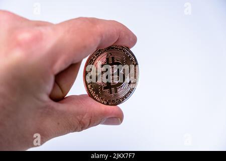 Männlicher Handfinger mit Bitcoin Kryptowährung Münze. Nahaufnahme einer Roségold-Bitmünze auf weißem Hintergrund. BTC beliebteste Krypto-Währung Mo Stockfoto