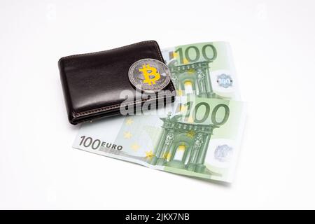 Bitcoin-Münze auf der Brieftasche mit zwei 100-Euro-Banknoten auf weißem Hintergrund. Bitcoin auf Brieftasche mit zweihundert Euro Banknoten. Stockfoto