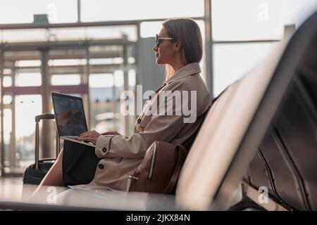 Geschäftsfrau mit Laptop und sitzt in der Wartehalle am Flughafen Stockfoto