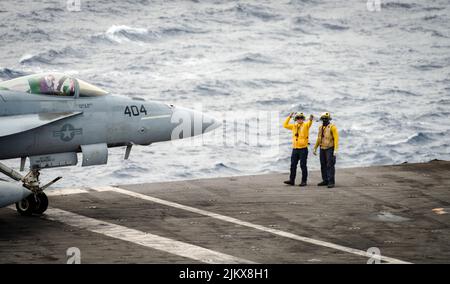 19. Juli 2022 - auf See - Aviation Boatswains Mate (Handling) 3. Klasse David Wilson, links, aus North Conway, New Hampshire, Und Aviation Boatswains Mate (Handling) Airman Randy Sumpter aus Charleston, South Carolina, leitet ein F/A-18E Super Hornet, das an den 'Dambustern' des Strike Fighter Squadron (VFA) 195 befestigt ist, das auf dem Flugdeck des einzigen vorwärts eingesetzten Flugzeugträgers der Marine, USS Ronald Reagan (CVN 76) landet. Die Dambuster erhielten ihren Spitznamen am 1. Mai 1951, als die Skyraiders der Staffel den schwer verteidigten und strategisch positionierten Hwacheon-Staudamm in Nordkorea mit einem zerstörten Stockfoto