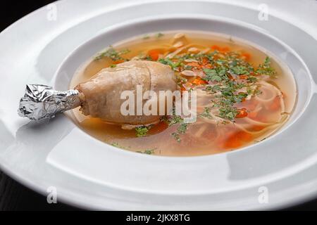 Hühnerbrühe mit Nudeln und Hühnerbein auf einem weißen Teller Stockfoto