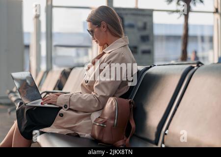 Junge Frau, die auf dem Laptop tippt und in der Wartehalle am Flughafen sitzt Stockfoto