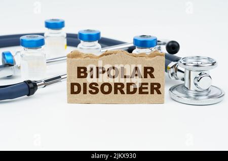 Medizin und Gesundheitskonzept. Auf einem weißen Tisch liegen Ampullen, ein Stethoskop und eine Pappe mit der Aufschrift - BIPOLARE STÖRUNG Stockfoto