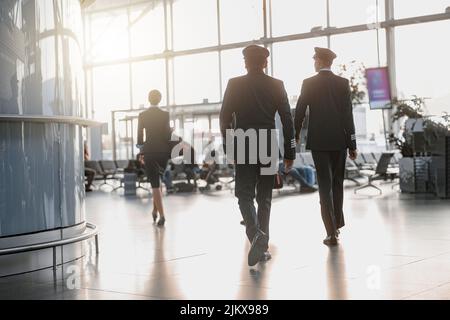 Zwei Piloten, die der Stewardess am Flughafenterminal entlang laufen Stockfoto