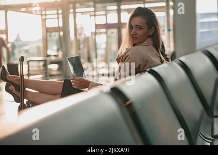 Schöne Frau, die mit einem Laptop arbeitet, während sie ihre Füße auf den Koffer legt Stockfoto