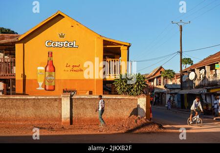 Ihosy, Madagaskar - 05. Mai 2019: Lokaler madagassischer Mann, der vor einem großen handbemalten Castel-Bier-Werbespot auf einer orangefarbenen Hauswand, typisch afrikanischer Stroe, läuft Stockfoto