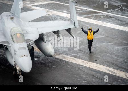 11. Juli 2022 - Philippine Sea - Aviation Boatswains Mate (Handling) 3. Klasse David Wilson aus North Conway, New Hampshire, leitet eine F/A-18E Super Hornet, die an das Dambusters of Strike Fighter Squadron (VFA) 195 auf dem Flugdeck des einzigen vorwärts eingesetzten Flugzeugträgers USS Ronald Reagan der US Navys befestigt ist (CVN 76). Die Dambusters erhielten ihren Spitznamen am 1. Mai 1951, als die Skyraiders der Staffel den stark verteidigten und strategisch platzierten Hwacheon-Staudamm in Nordkorea mit Lufttorpedonen durch präzise Niederlagen zerstörten. Ronald Reagan, das Flaggschiff von Carrier Strike Stockfoto