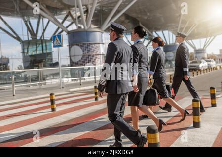 Zwei Flugbegleiter und männliche Piloten gehen in einer Reihe, während sie die Straße überqueren Stockfoto