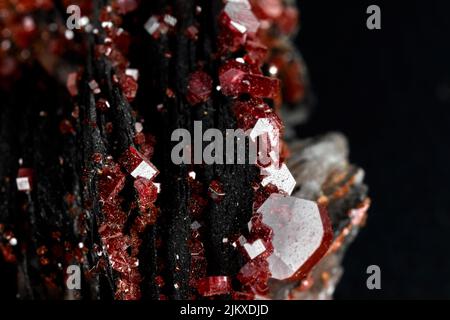 Eine Nahaufnahme von kleinen seltenen roten Mineralien auf einem schwarzen unscharfen Hintergrund Stockfoto