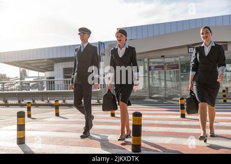 Zwei Flugbegleiter mit Taschen und ihr Kollege, der die Straße überquert Stockfoto