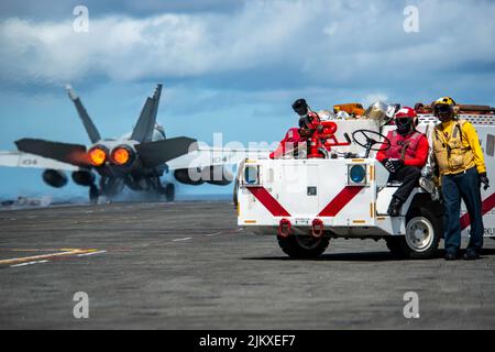 11. Juli 2022 - Philippinische See - Seeleute beobachten eine F/A-18F Super Hornet, die an den 'Diamondbacks' des Strike Fighter Squadron (VFA) 102 Starts vom Flugdeck des einzigen vorwärts eingesetzten Flugzeugträgers der US Navy USS Ronald Reagan (CVN 76) angebracht ist. Die Diamondbacks führen Carrier-basierte Luftangriff- und Streikkräfte-Escort-Missionen sowie Schiff-, Kampfgruppen- und Geheimdiensteintreibemissionen durch. Ronald Reagan, das Flaggschiff der Carrier Strike Group 5, stellt eine kampfbereite Truppe bereit, die die Vereinigten Staaten schützt und verteidigt, und unterstützt Allianzen, Partnerschaften und kollektive maritime Inte Stockfoto