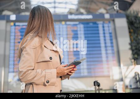 Junge Frau mit Smartphone, die die Informationskarton am Flughafen ansieht Stockfoto